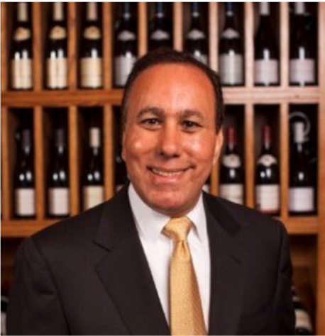 A man in suit and tie standing next to wine bottles.