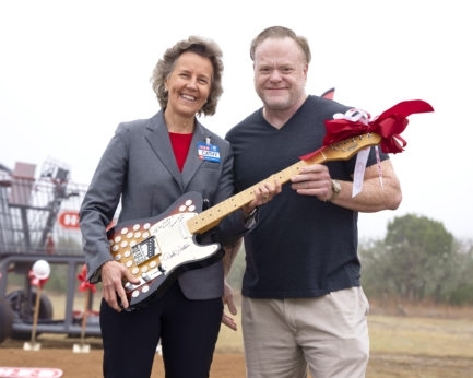 A man and woman holding a guitar in front of a helicopter.