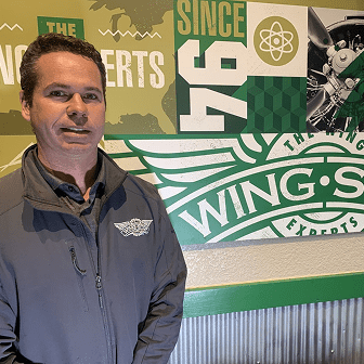 Man standing in front of Wing Experts sign.