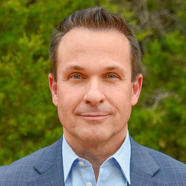 Man in suit with green foliage background.