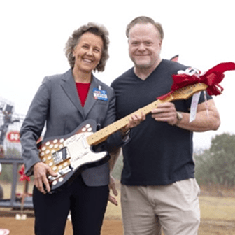 Two people holding a decorative guitar outdoors.
