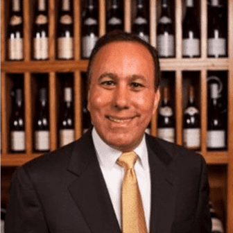 Man in suit smiling in wine cellar.