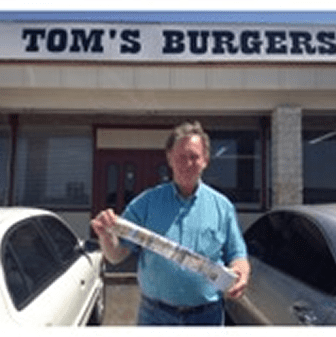 Man holding item outside Tom's Burgers restaurant.
