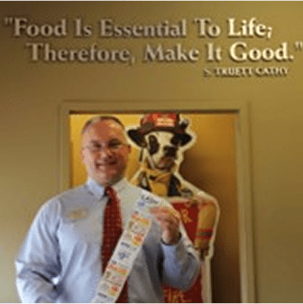 Man holding coupons, quote on wall behind.