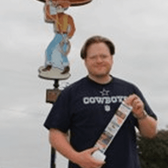 Man holding photos near cowboy statue.