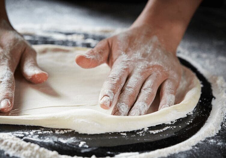 Hands shaping dough on a floured surface.